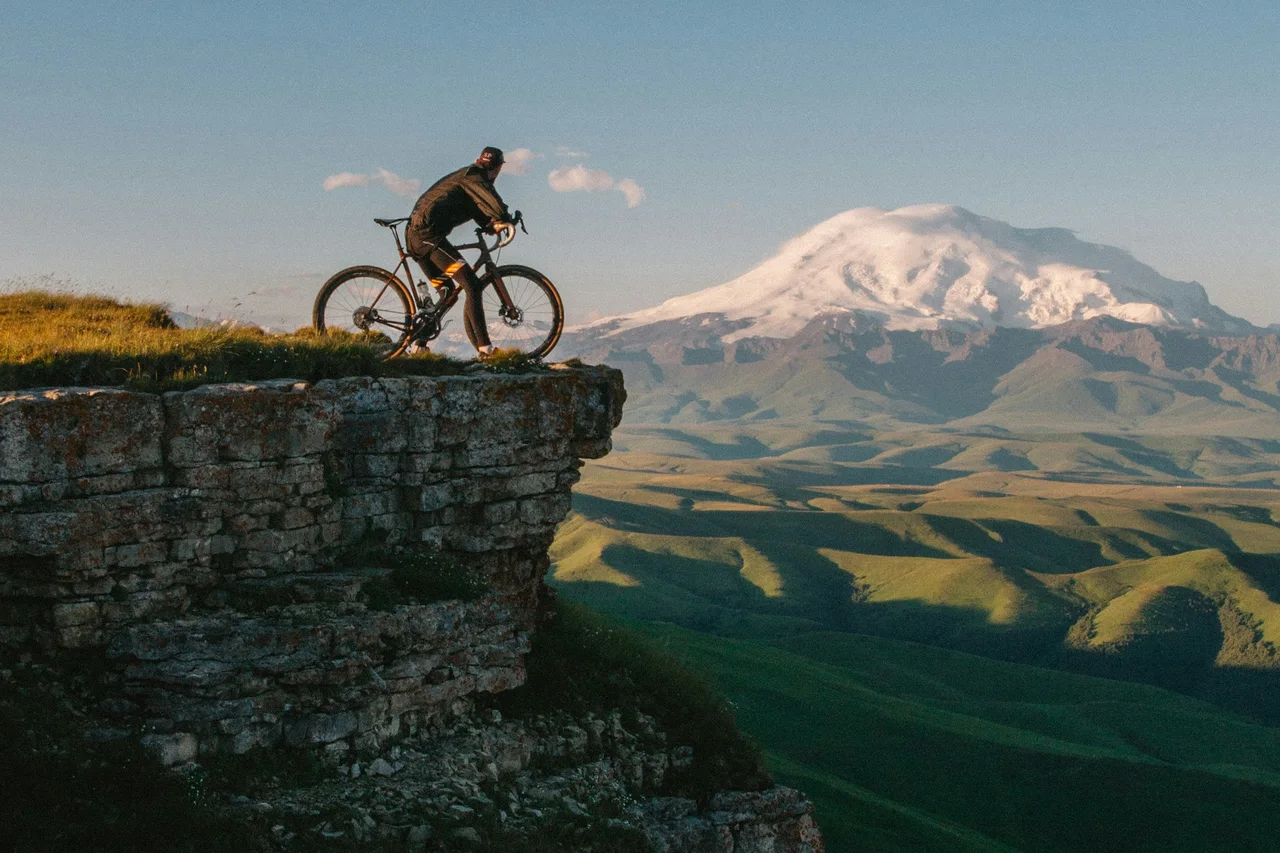 A cyclist on a rocky ridge above a green mountain valley