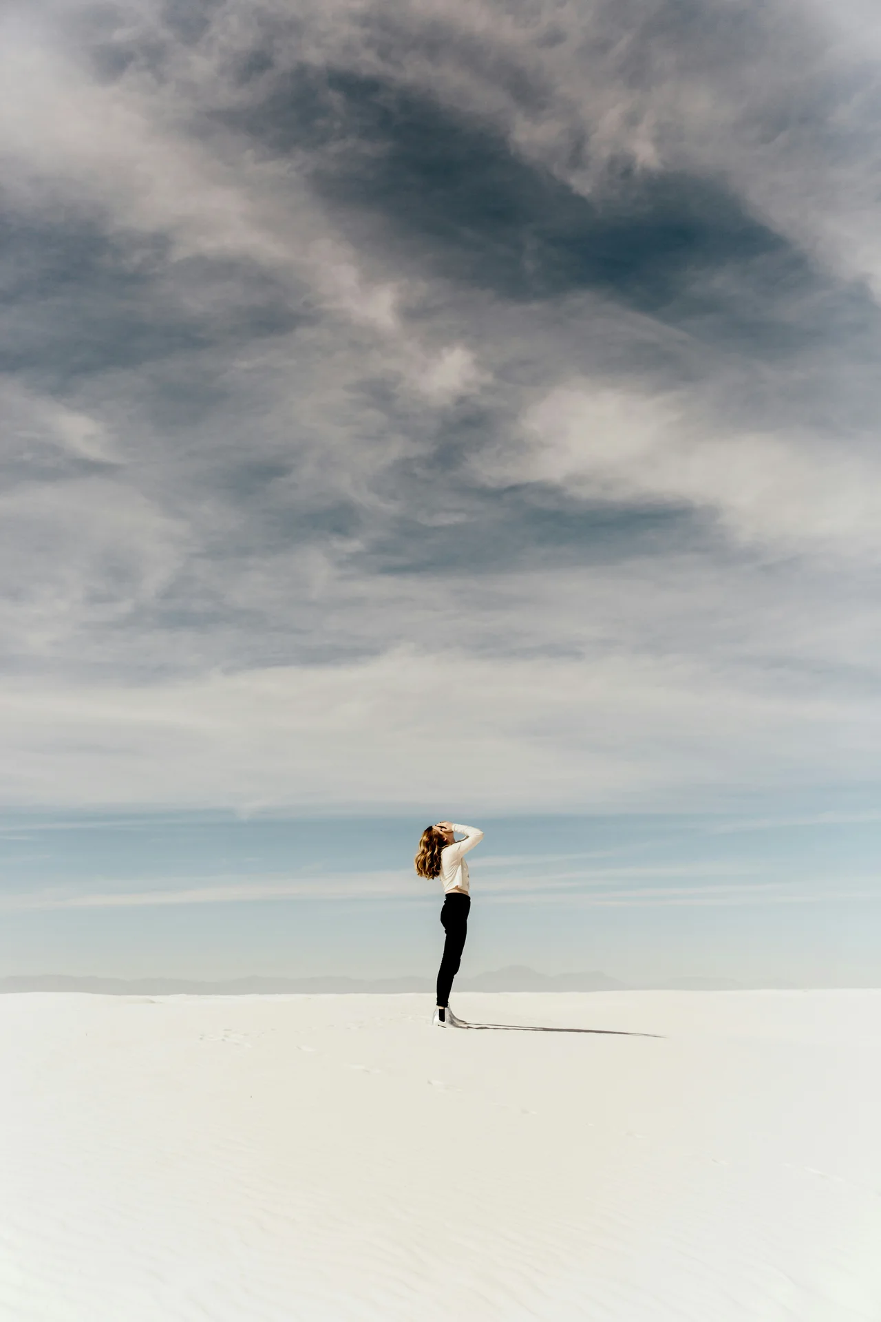 A lone figure beneath a wide, cloud-filled sky