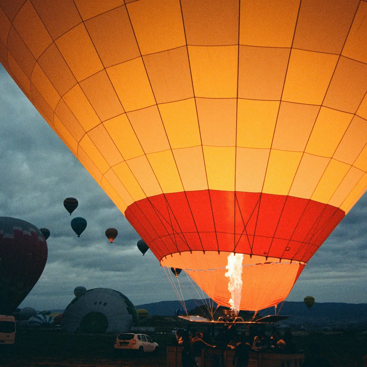 An orange hot air balloon illuminated by its burner before takeoff