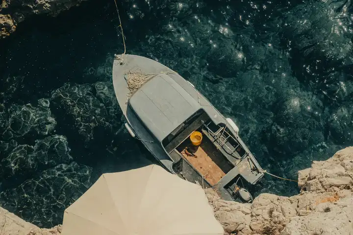 A small boat beside a rocky coast and a white sun umbrella