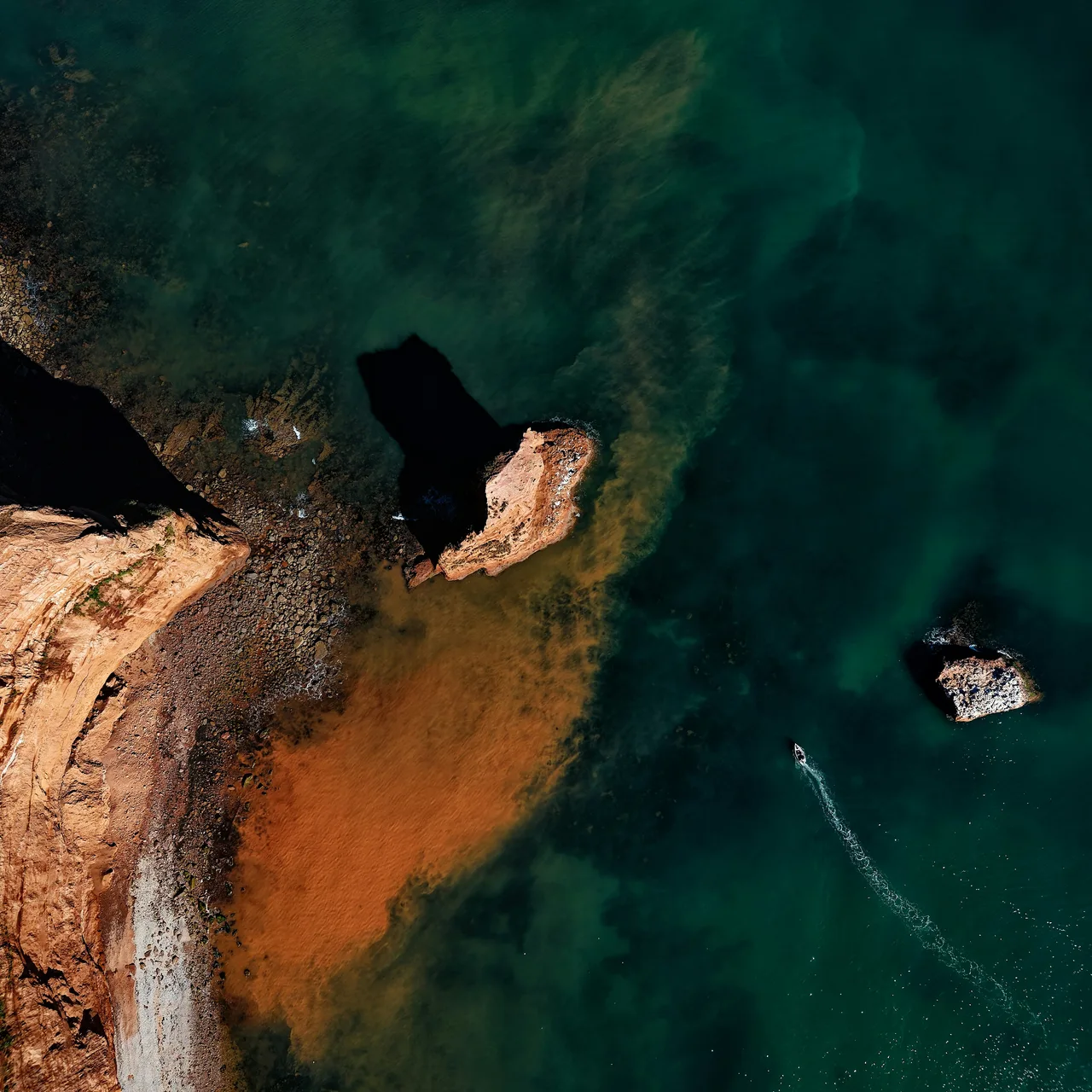 An aerial view of rust-coloured rocks surrounded by deep green seawater