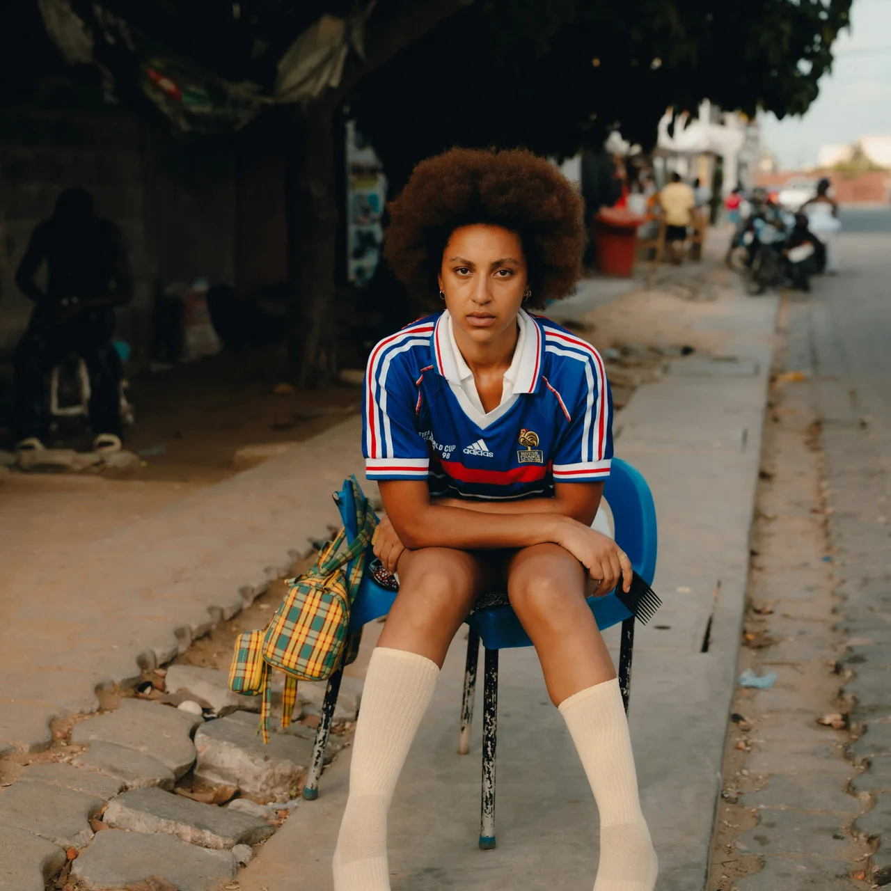 A woman in a blue striped sports shirt sitting beside a cobbled street