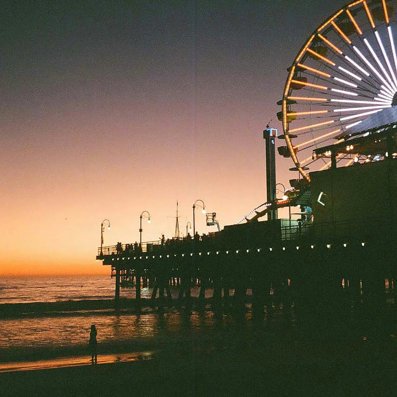 A Ferris wheel and pier silhouetted against an orange seaside sunset