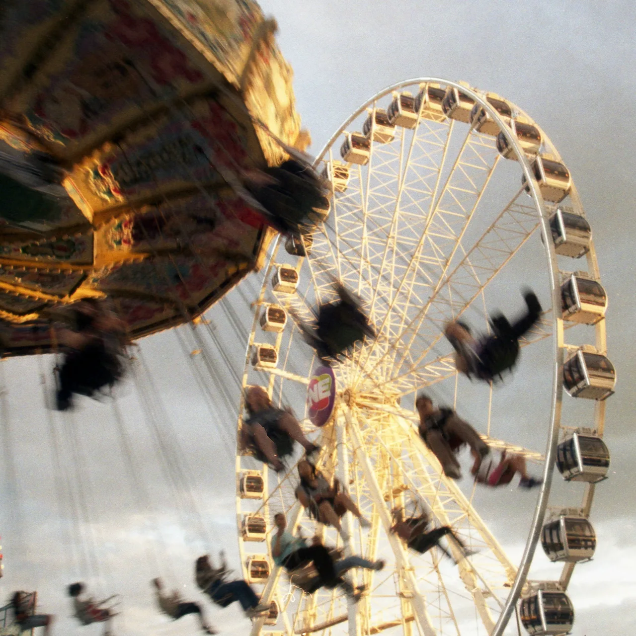 Blurred swing riders passing in front of a large Ferris wheel