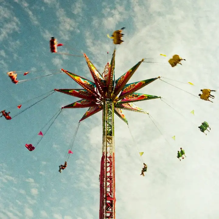 Riders circling a colourful star-shaped fairground swing against a cloudy sky