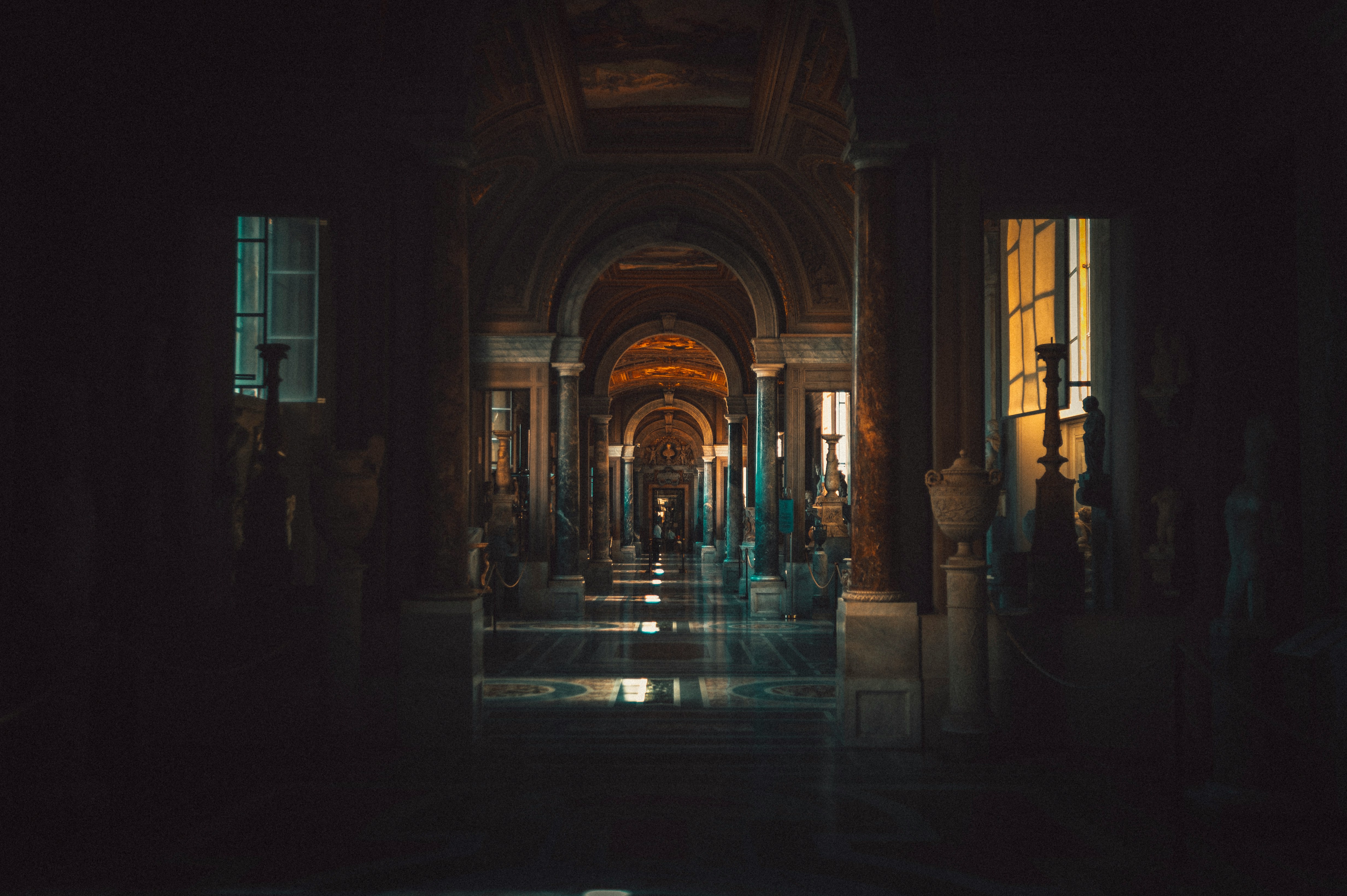 A figure in orange walking through an ancient stone colonnade