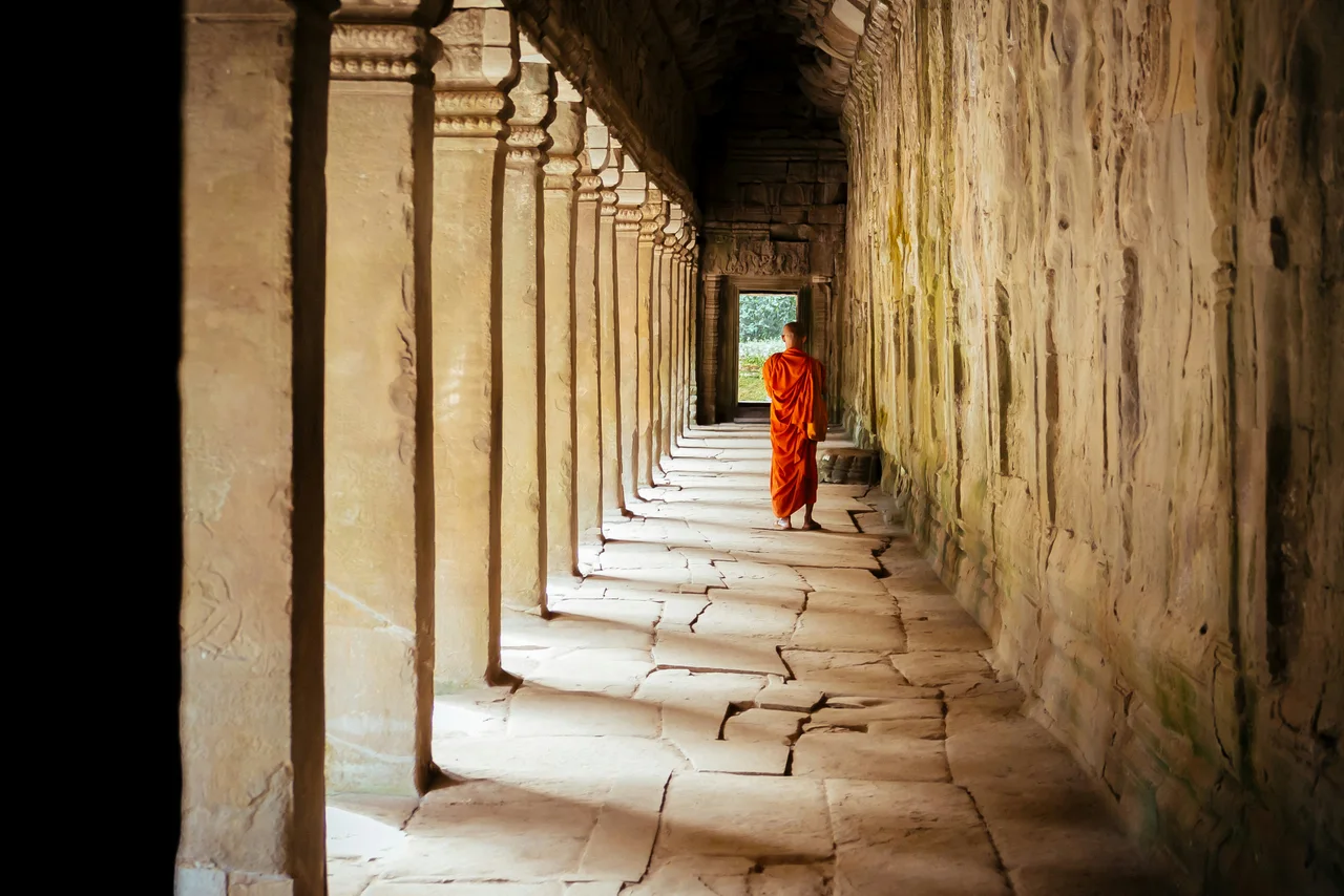 A figure in orange walking through an ancient stone colonnade