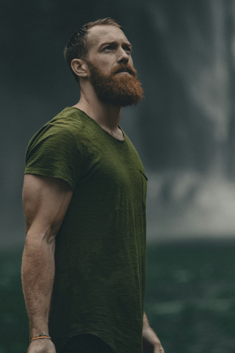 A man in a green shirt looking upward in a forest