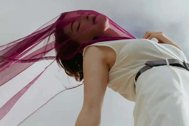 A woman in white with a flowing pink scarf photographed from below