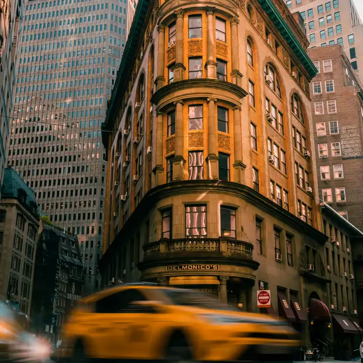 A yellow taxi passing an ornate orange building between city towers
