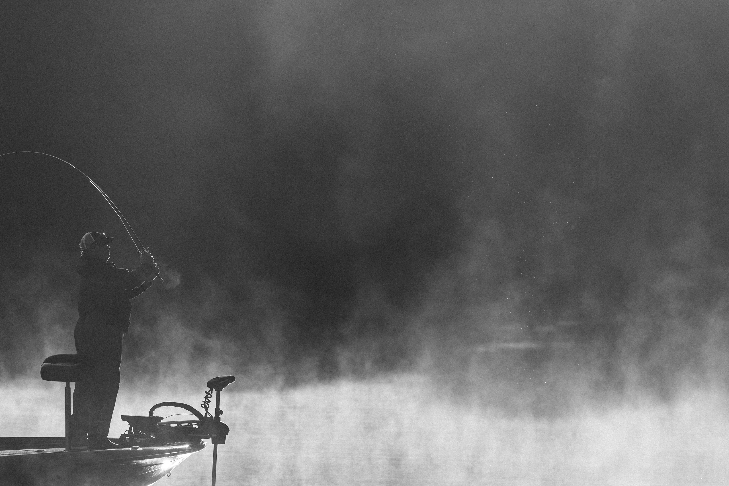 Silhouette of a fisherman casting a line into morning mist, in black and white