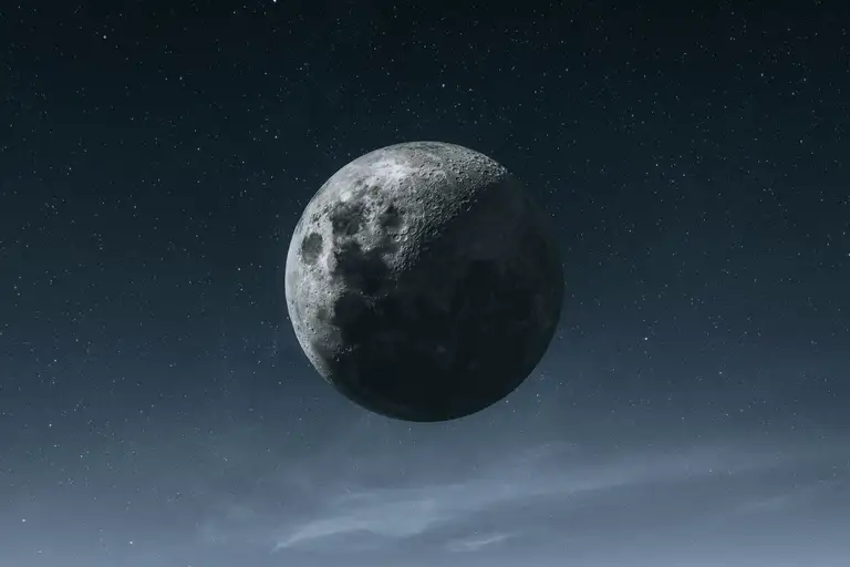 Crescent moon hanging in a dark starry sky above a thin band of cloud