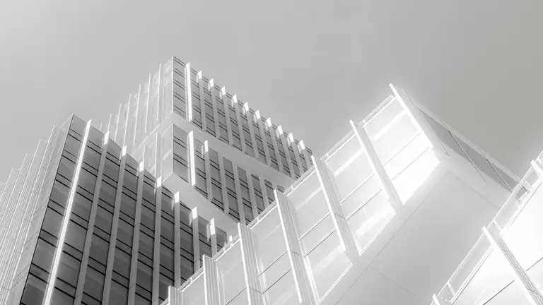 Low angle view of a glass tower's angular facades against a pale sky
