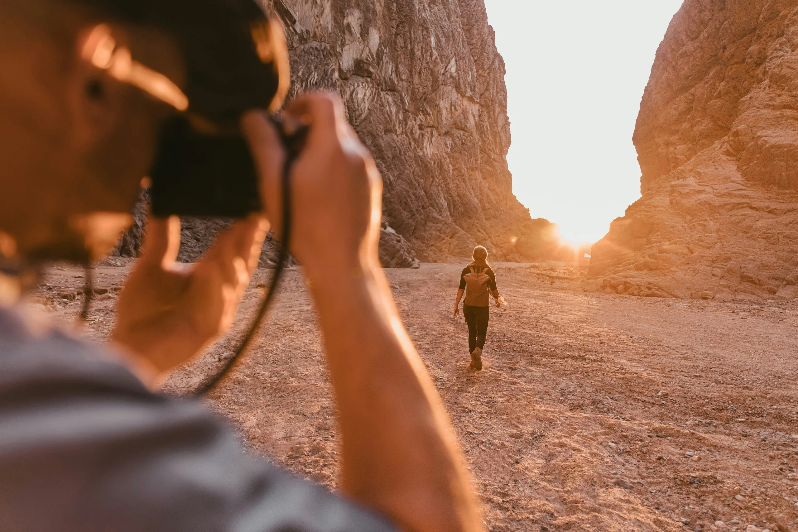 Lone hiker at the foot of towering sandstone canyon walls in warm light