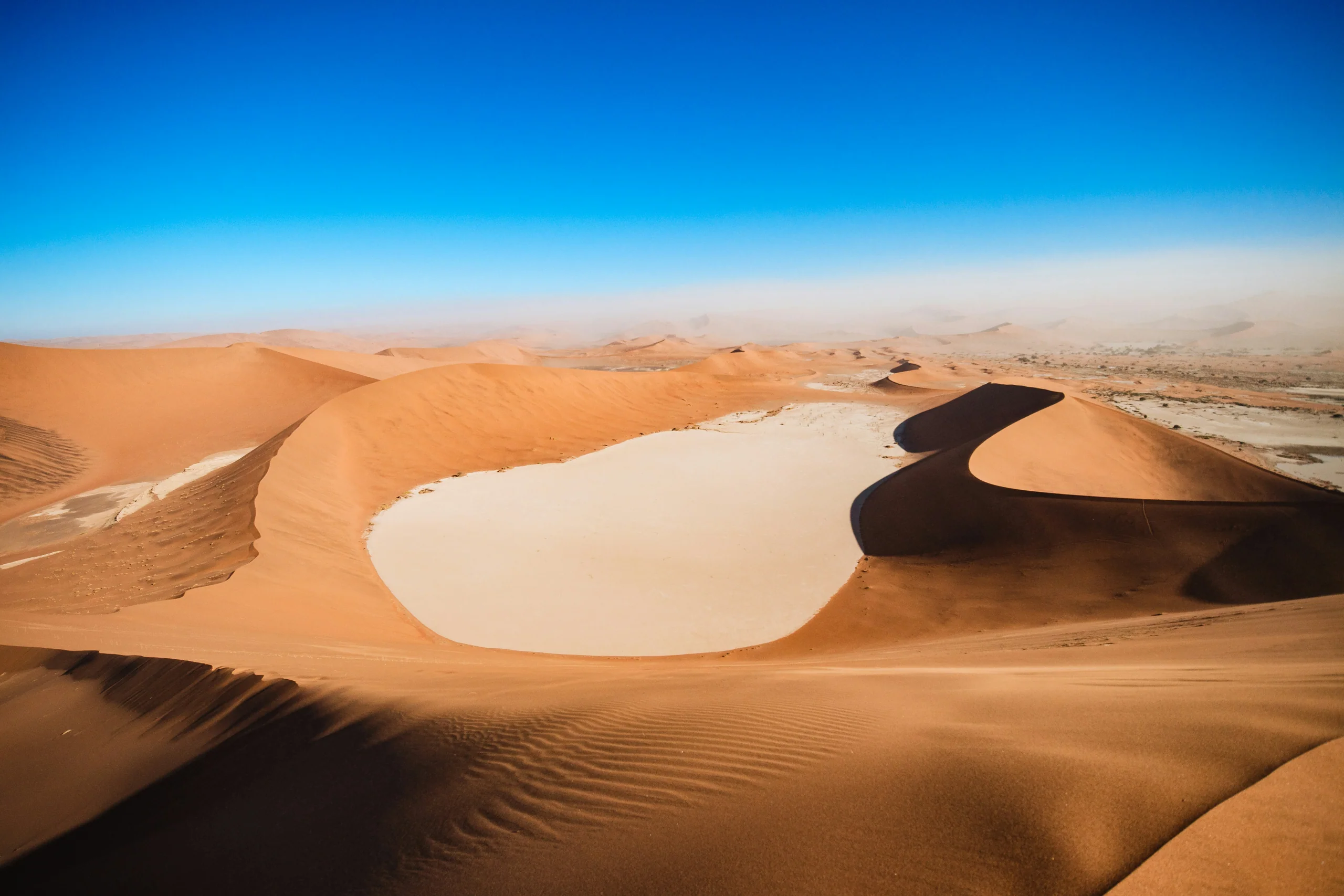 Rippled sand dunes under a clear blue sky in soft desert light