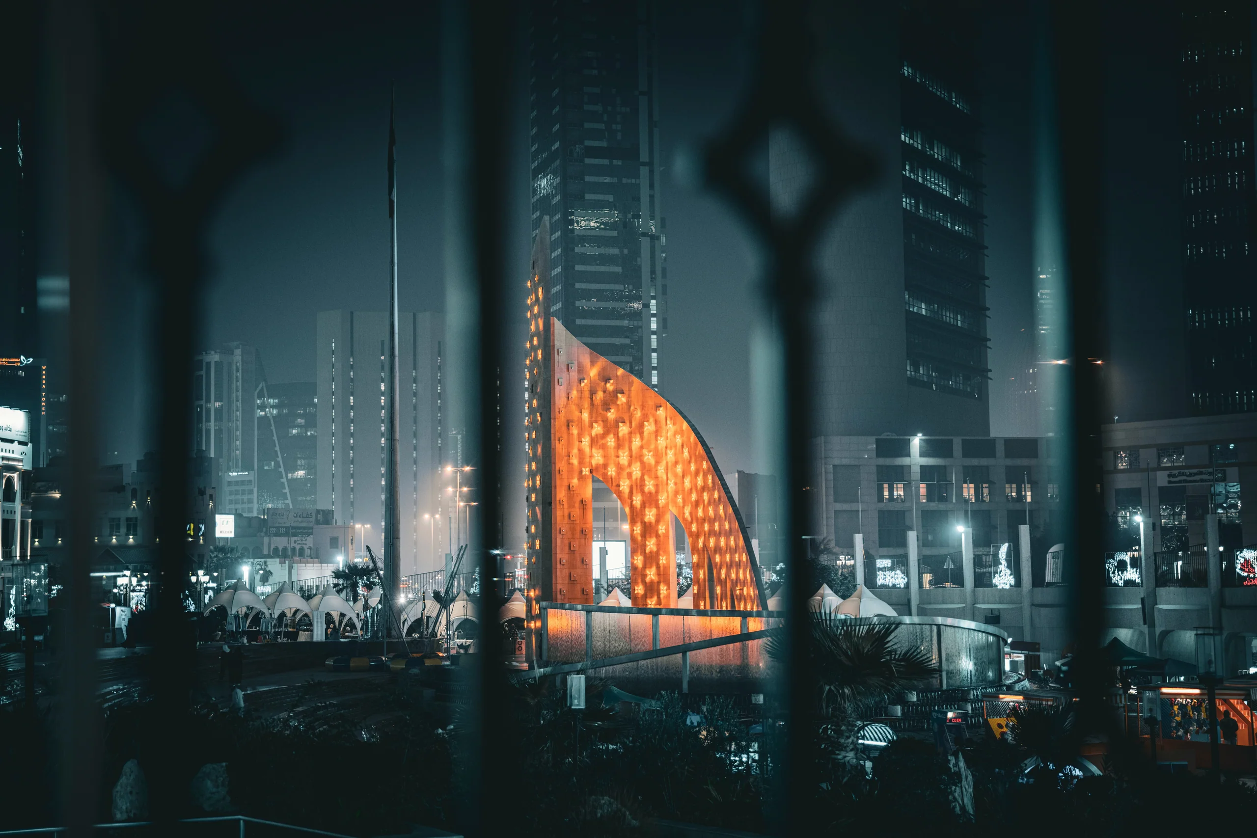 City street at night with a lit orange sculpture between towers