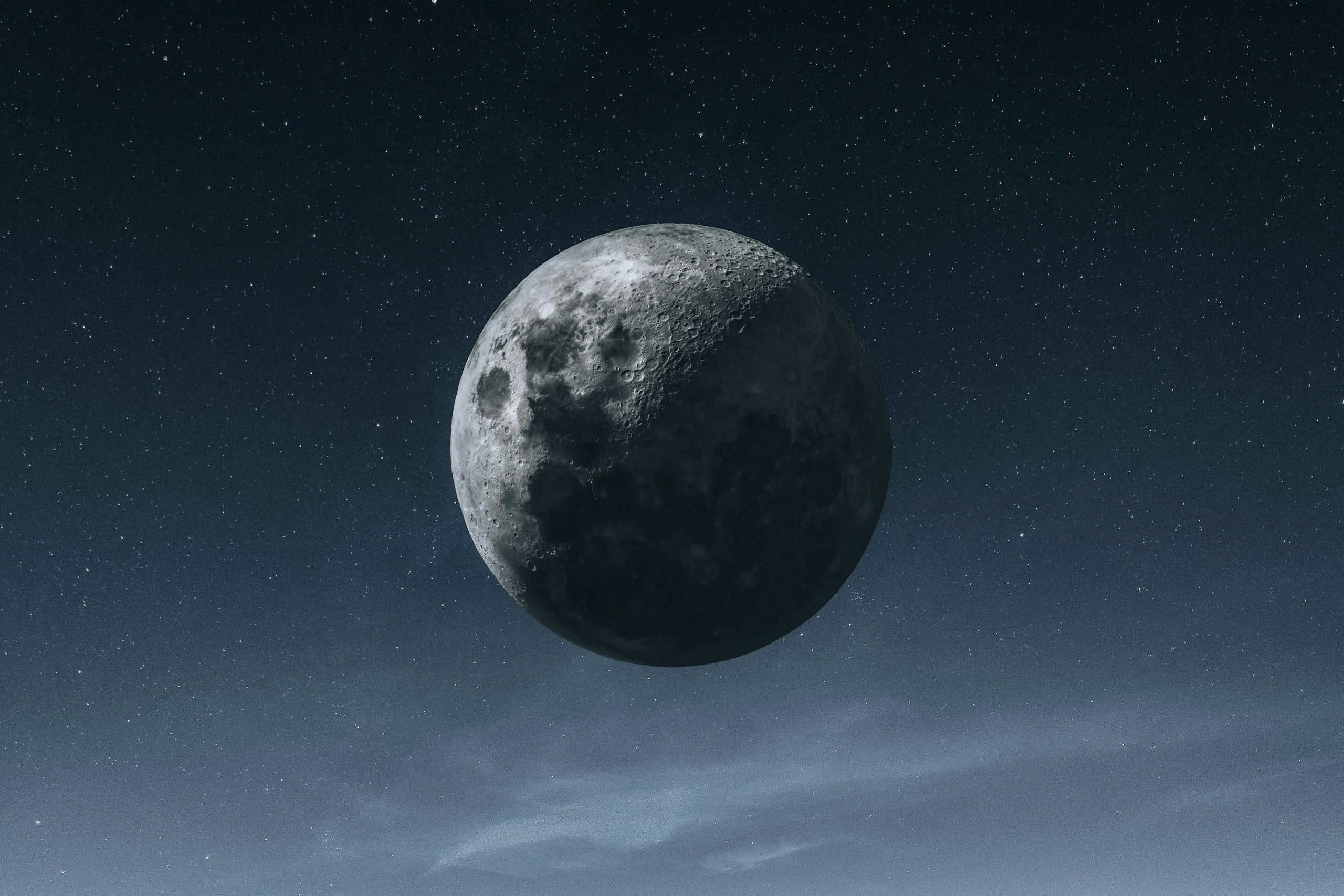 Crescent moon hanging in a dark starry sky above a thin band of cloud