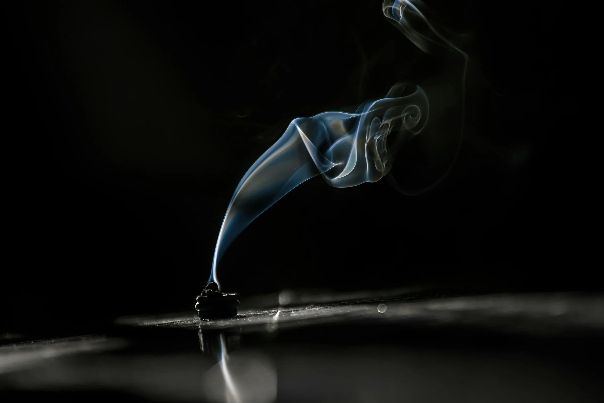 Thin trail of incense smoke rising against a black background